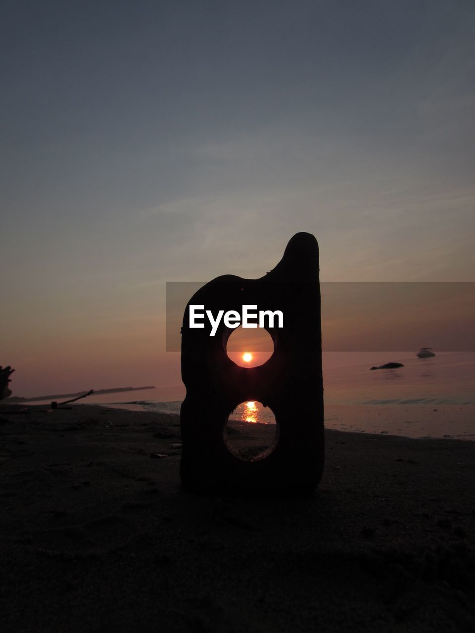 ILLUMINATED LAMP ON BEACH AGAINST SKY DURING SUNSET