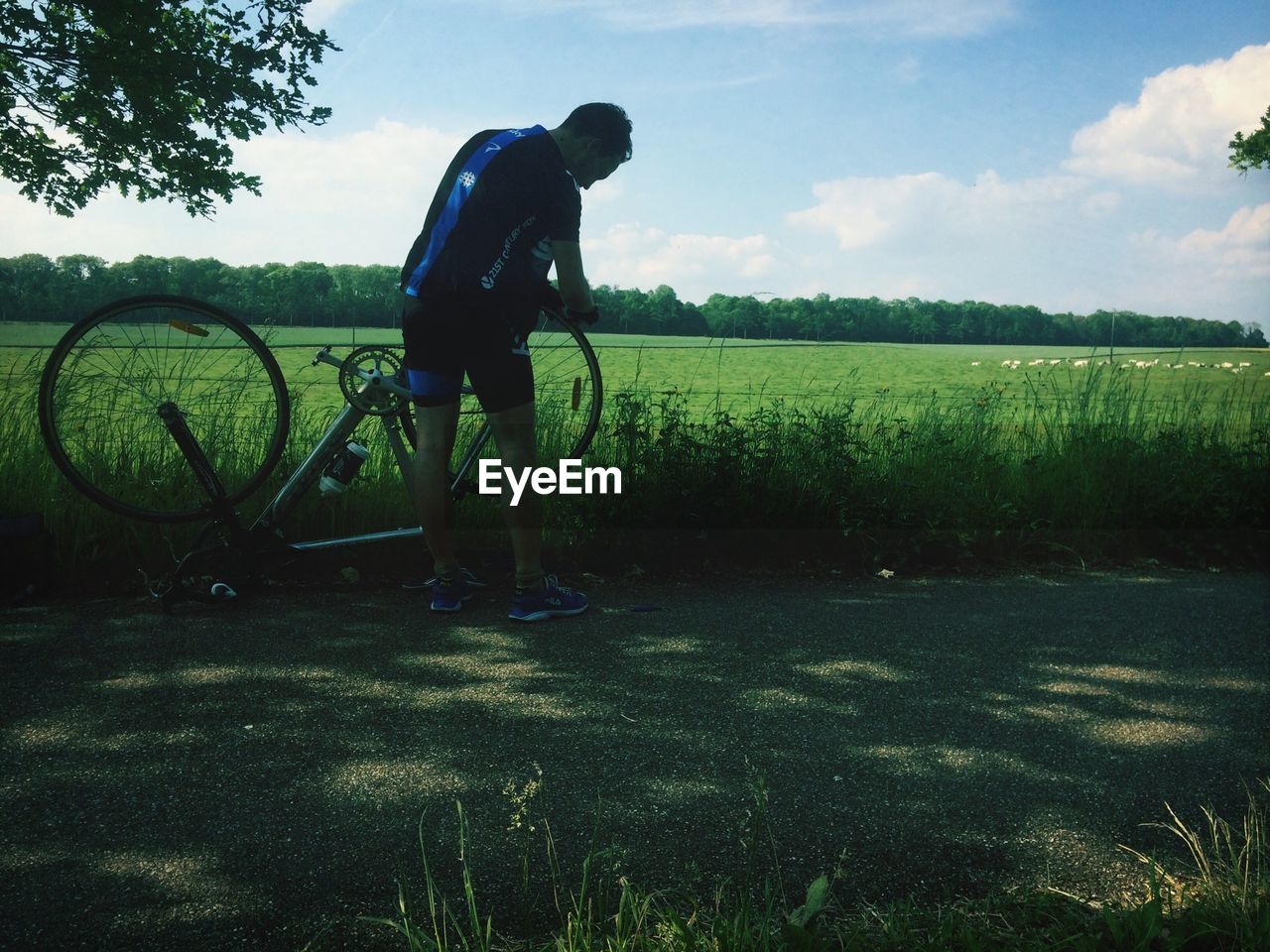 Full length rear view of man repairing bicycle on country road