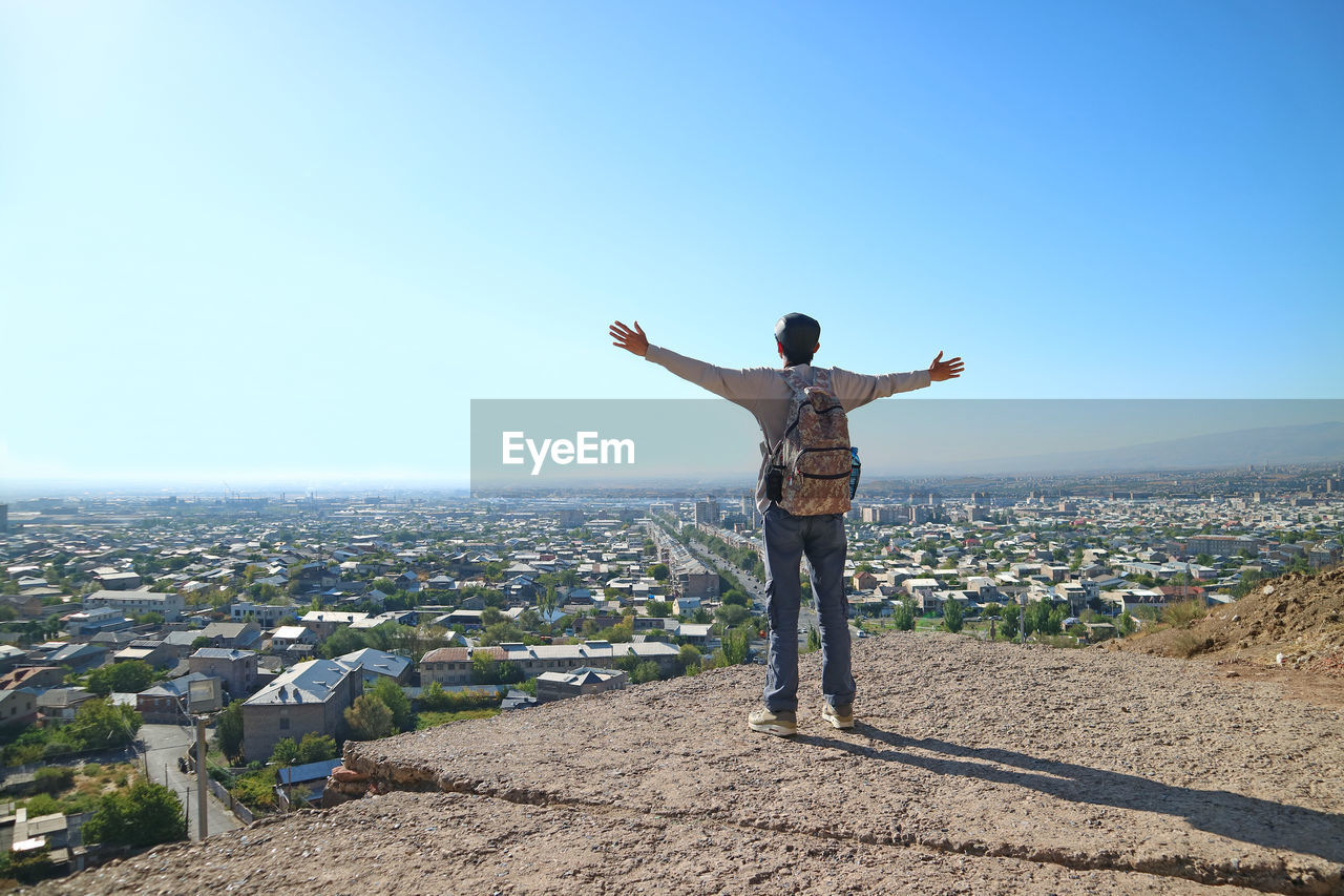 Rear view of man with arms outstretched standing against sky