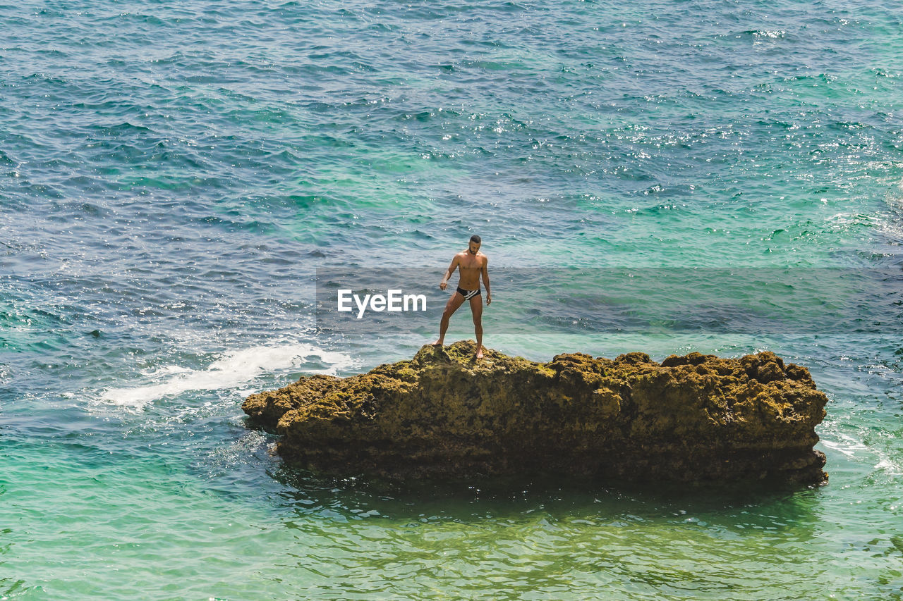 MAN STANDING ON ROCK AT SEA SHORE