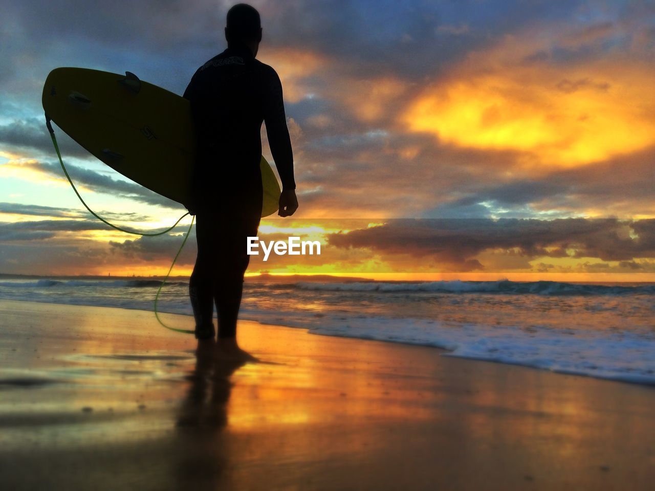 Low angle view of silhouette man with surfboard standing on beach