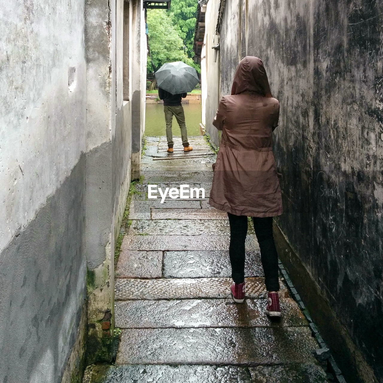 Rear view of man and woman standing on alley amidst houses during rainy season
