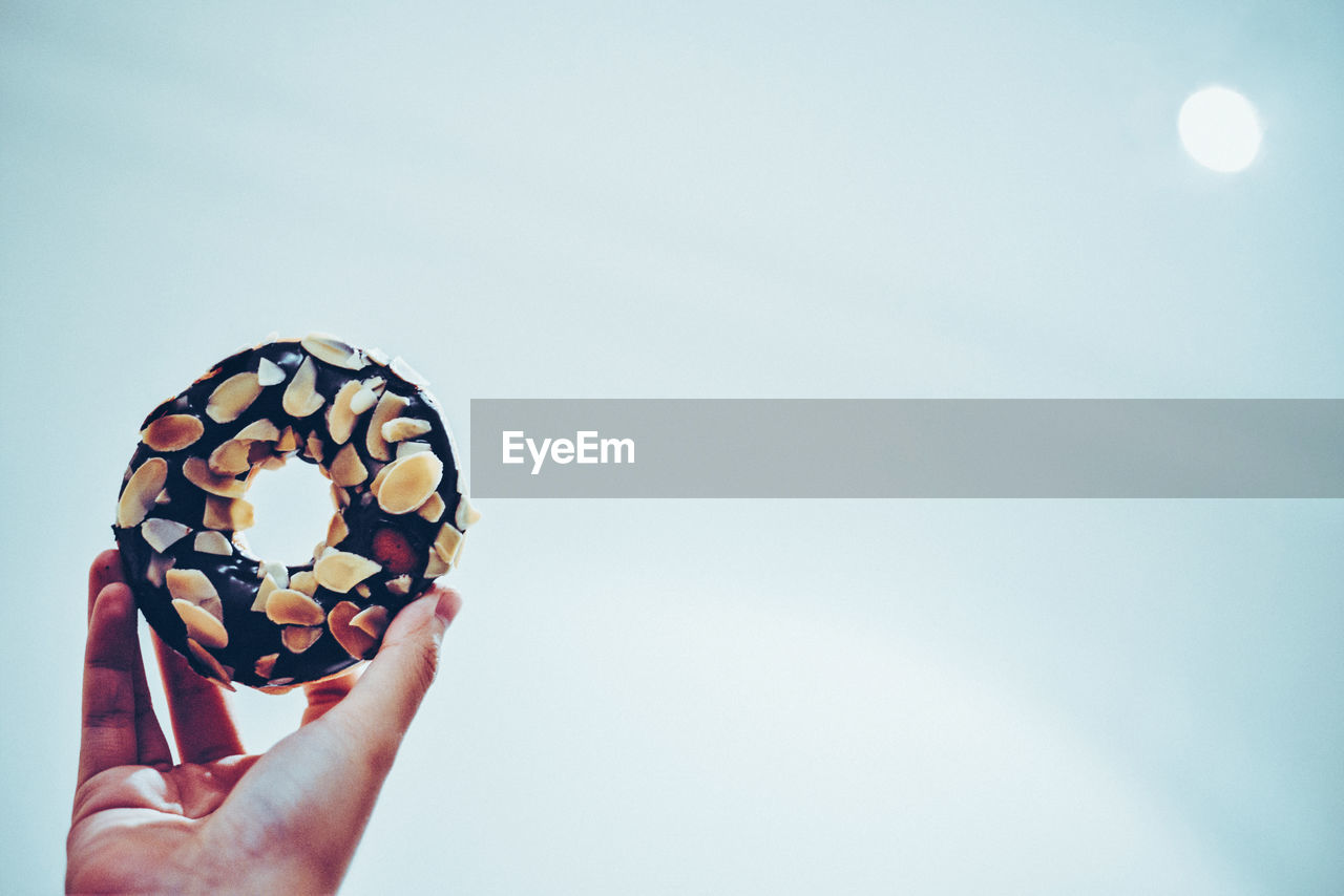 Close-up of hand holding donut against sky