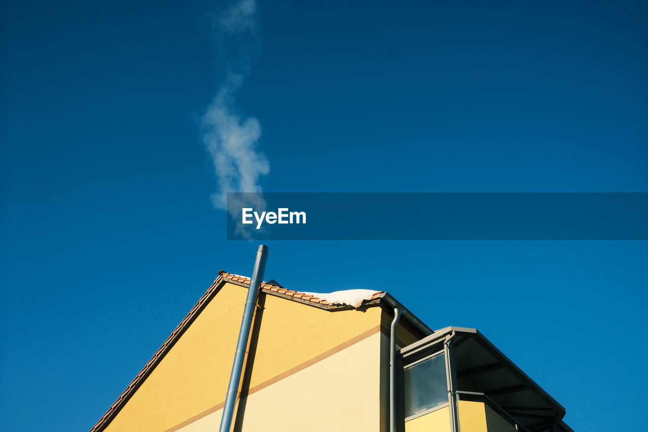 Low angle view of smoke emitting from chimney against clear blue sky