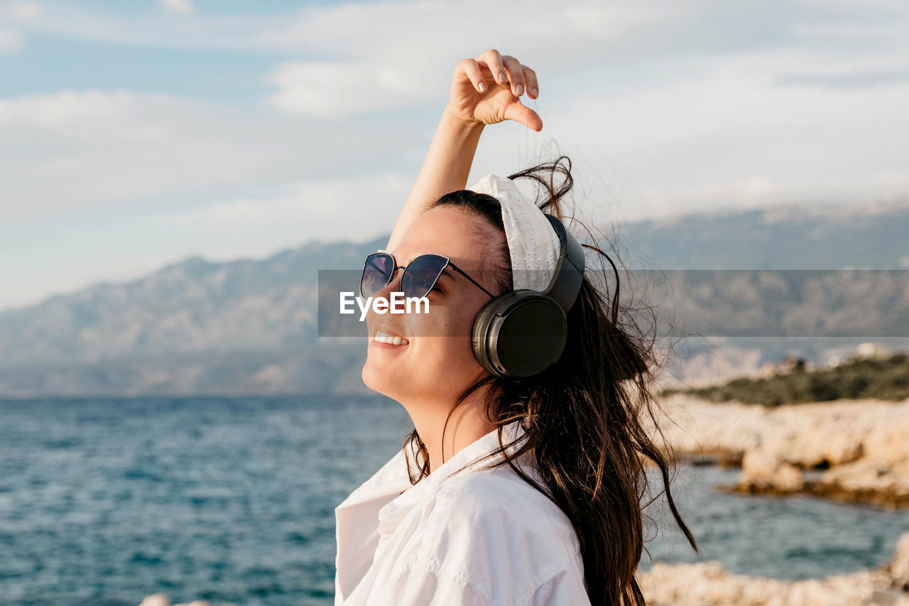 Side view of young woman in white shirt listening to music on headphones. summer, beach, lifestyle.