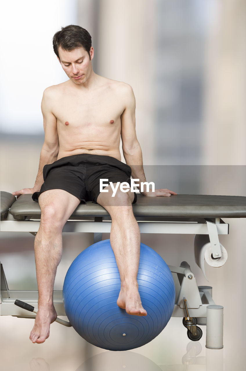 Shirtless man sitting on massage table in spa