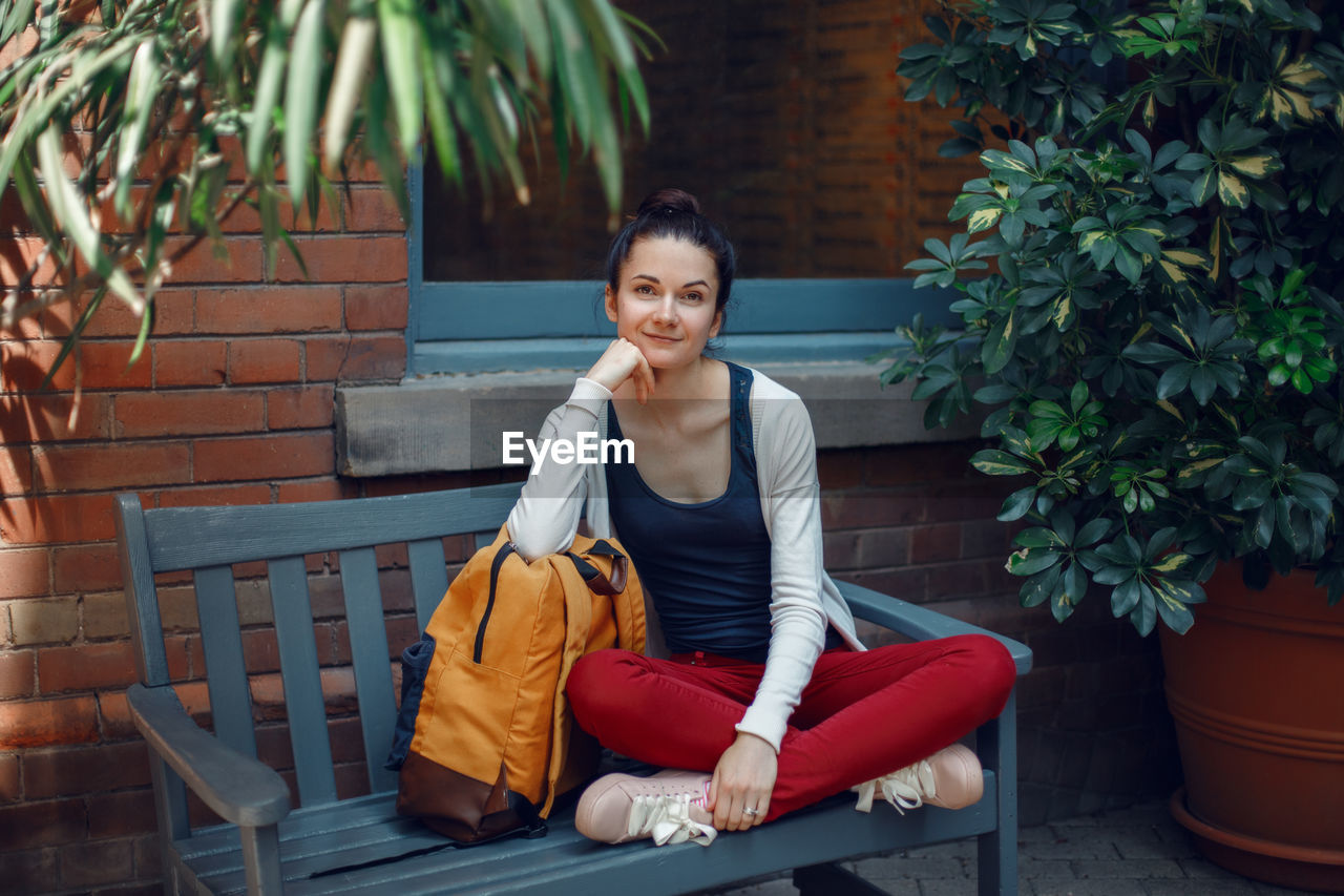 Portrait of smiling woman sitting on bench against plants