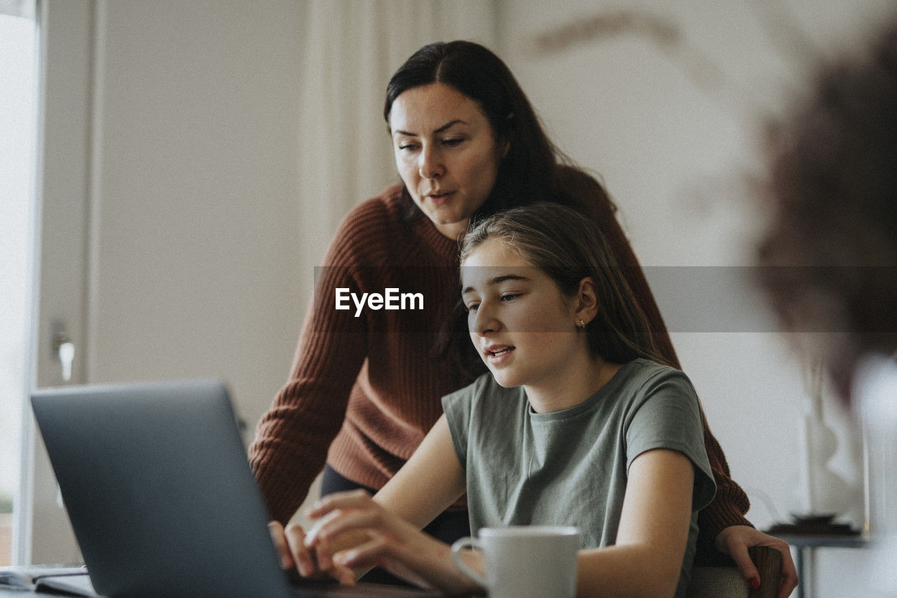Girl using laptop sitting by mother at modern home