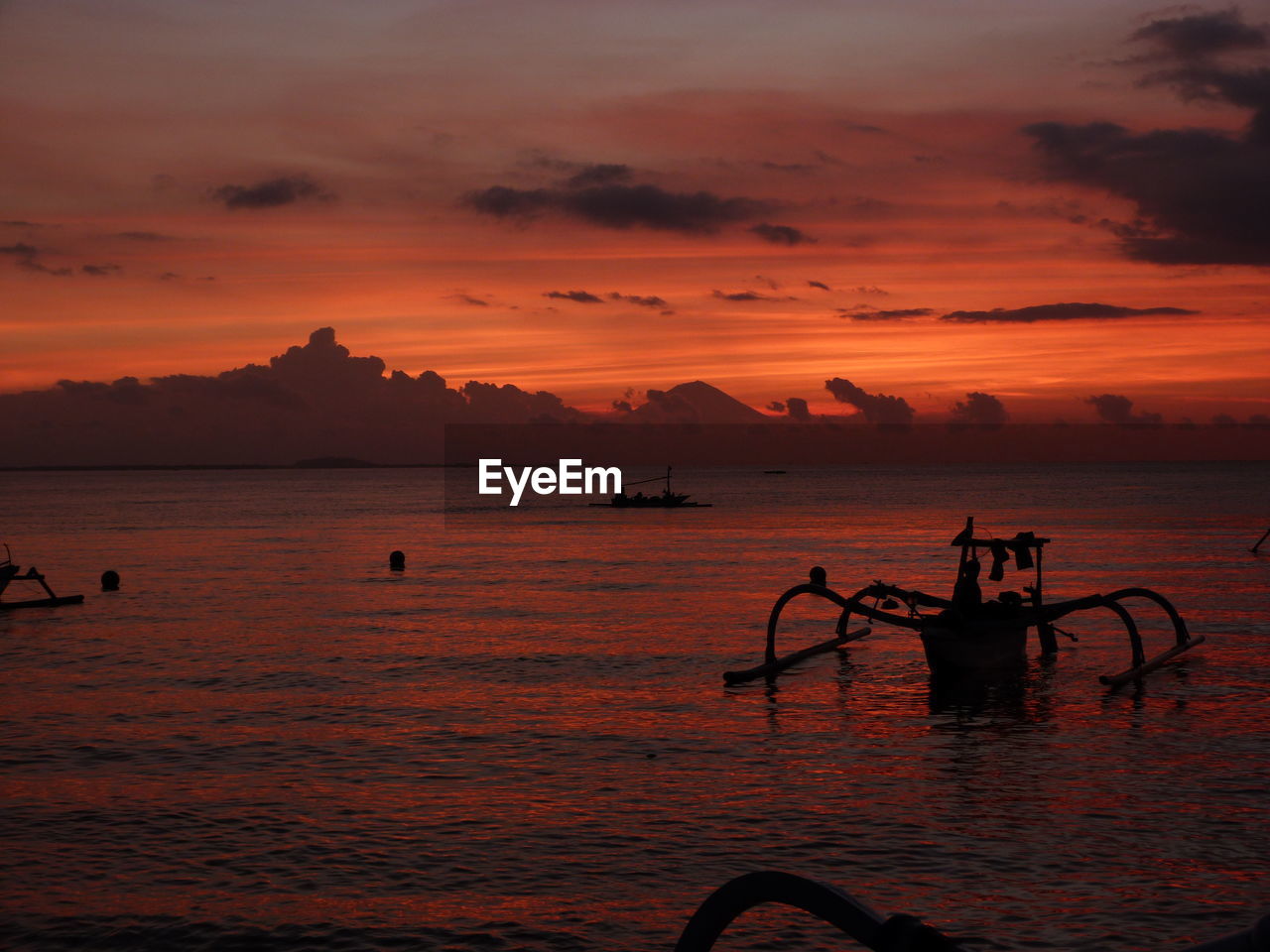 Silhouette outrigger boat moored in sea against sky during sunset