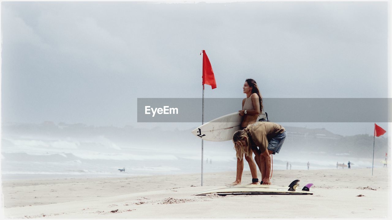 Full length of surfers on beach against sky