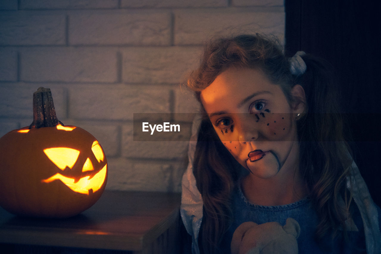 Cute girl wearing costume standing by pumpkin during halloween