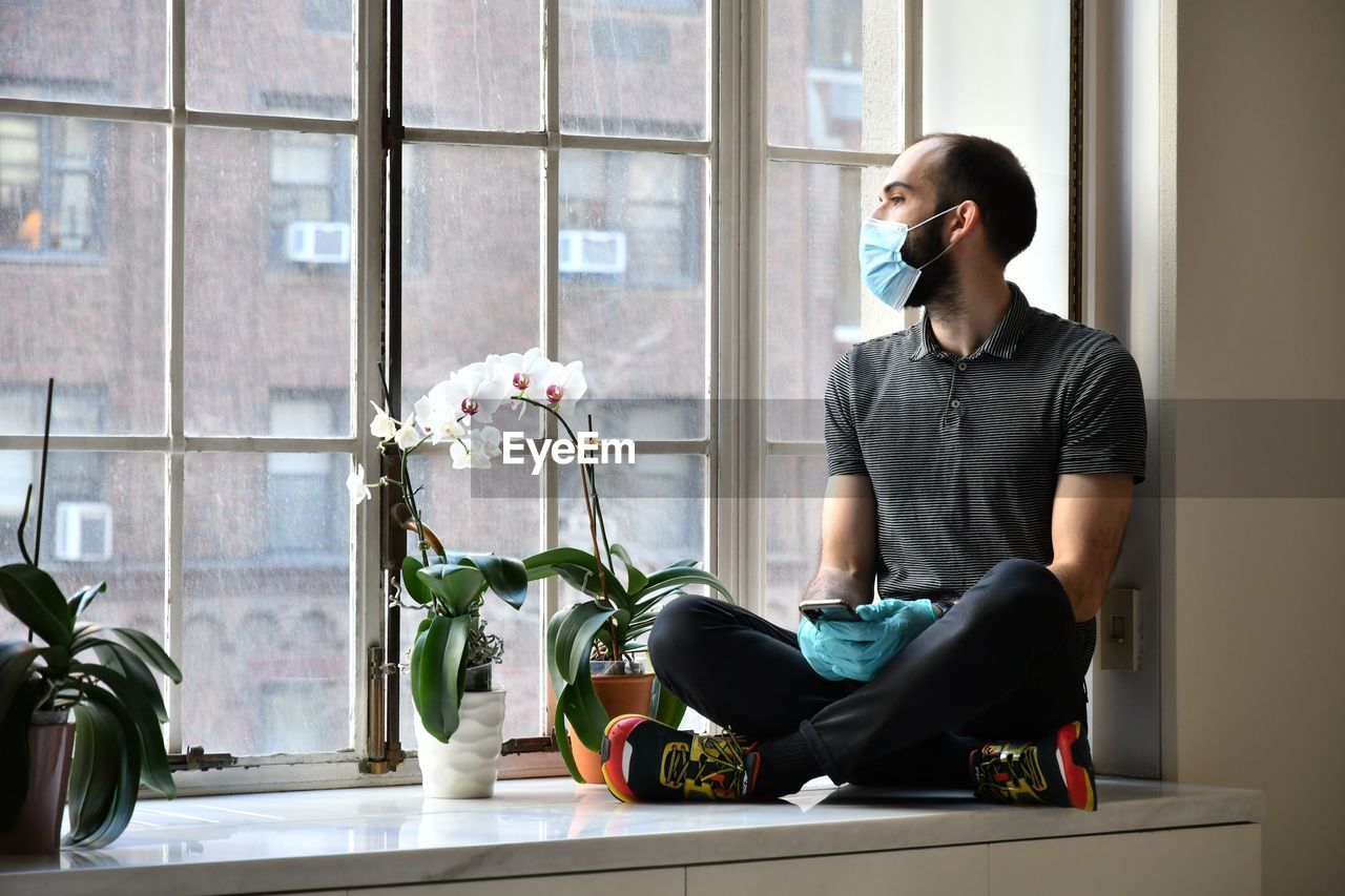 Full length of man sitting by window at home