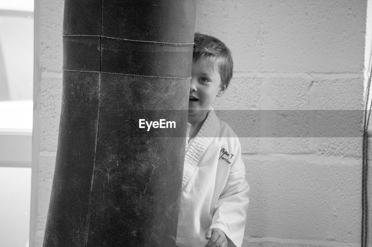 Portrait of boy in sport clothing behind punching bag at martial arts classroom
