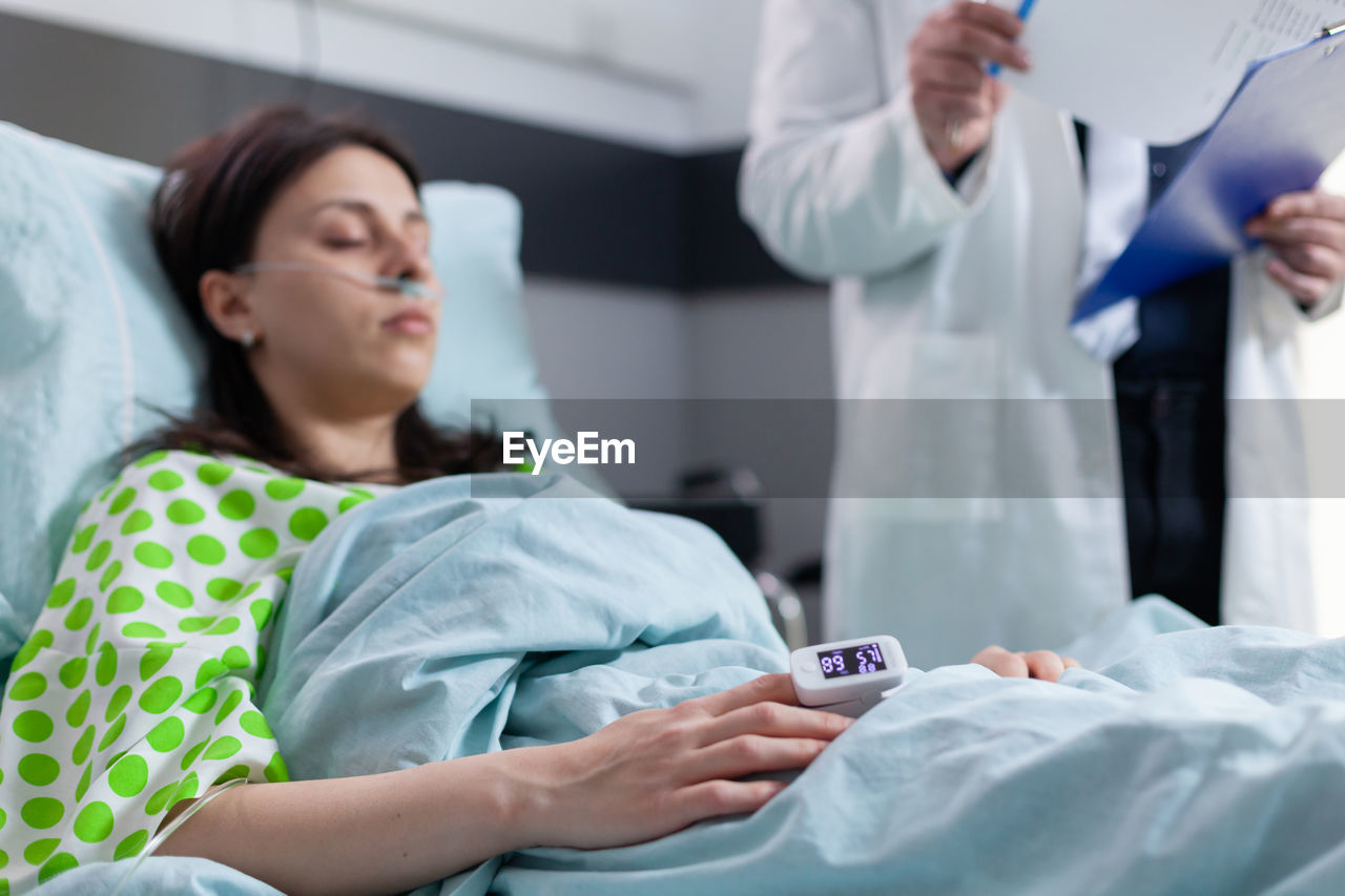 Woman lying on bed with pulse oxymeter in hand