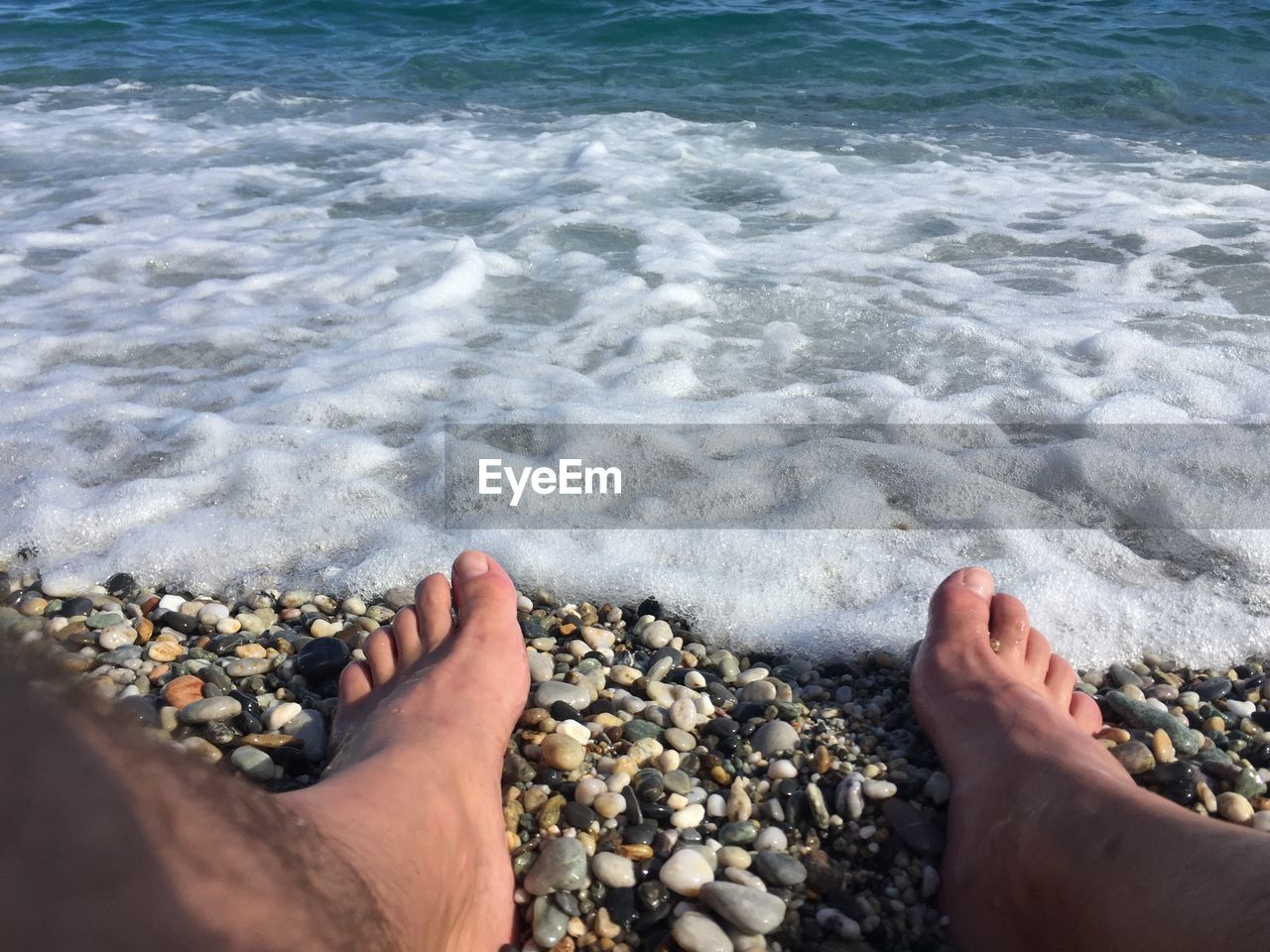 Low section of man sitting on pebbles at beach