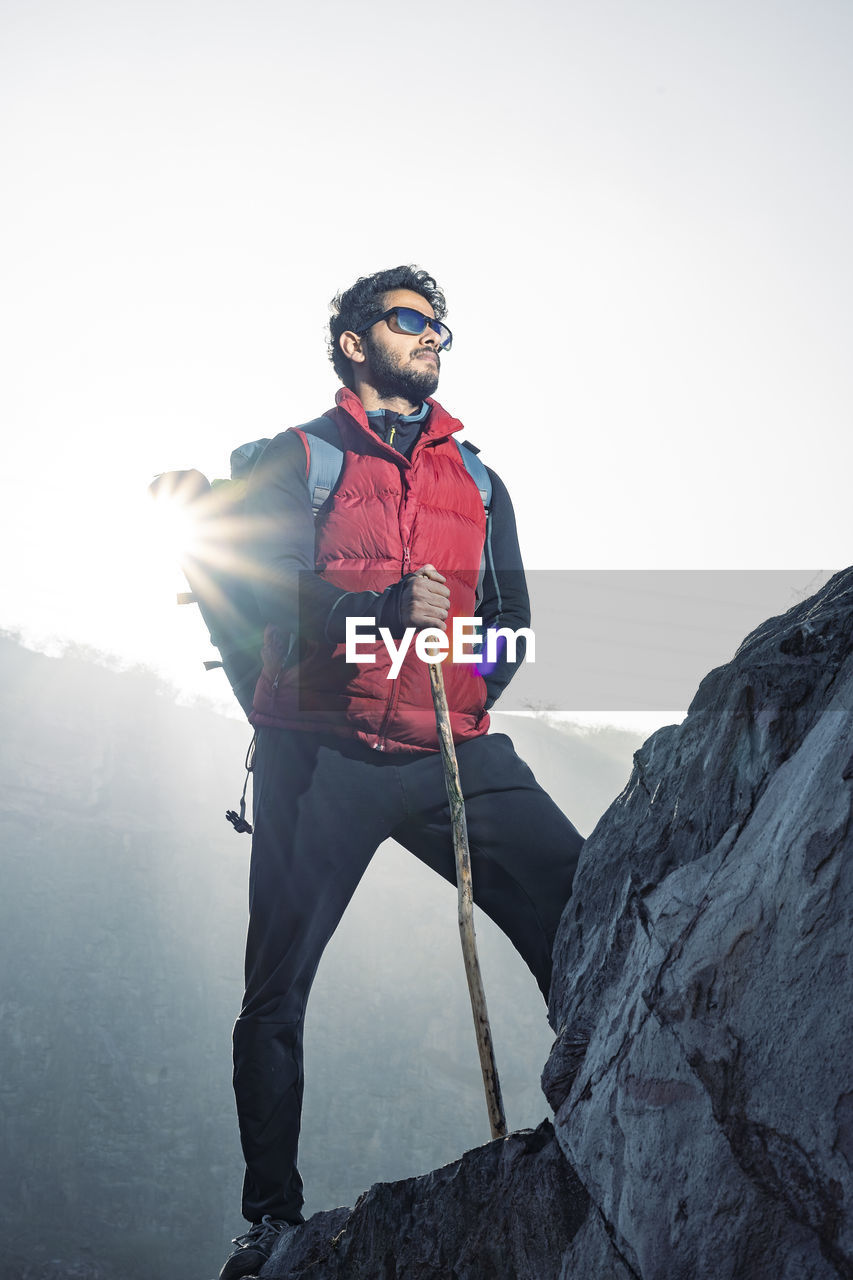 Young indian traveler boy trekking over a rocky mountain, standing on the top of the mountain.