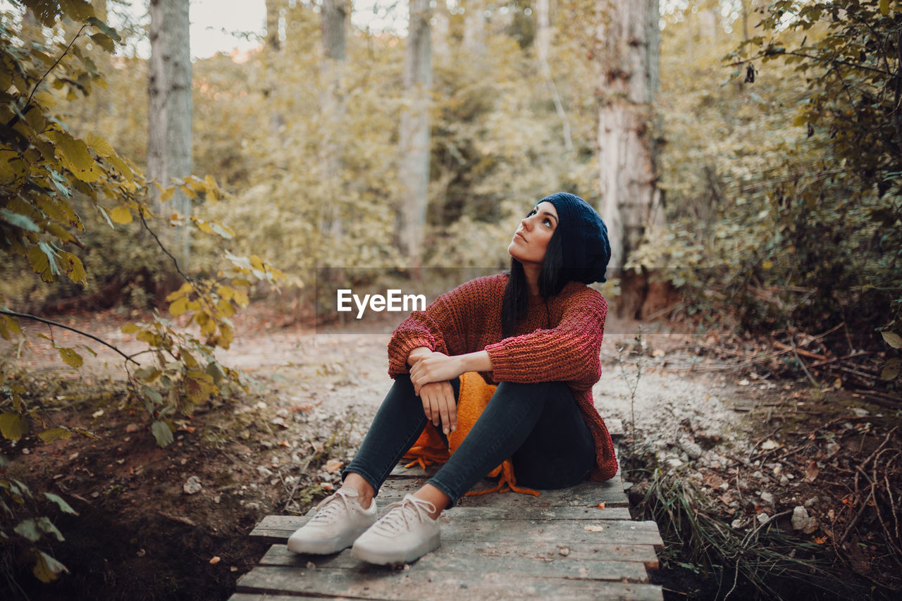 Full length of young woman sitting on street amidst trees in forest