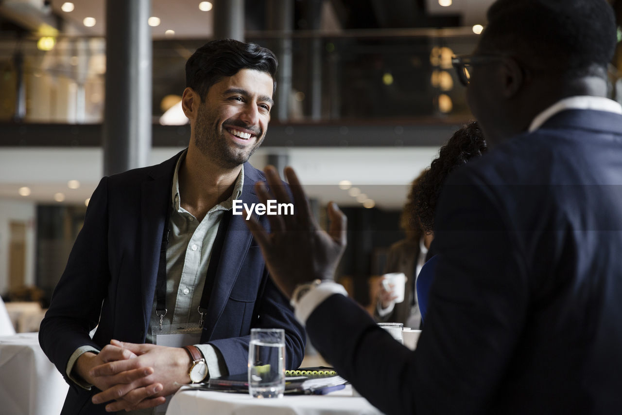 Happy businessman leaning on table while talking with entrepreneur at seminar