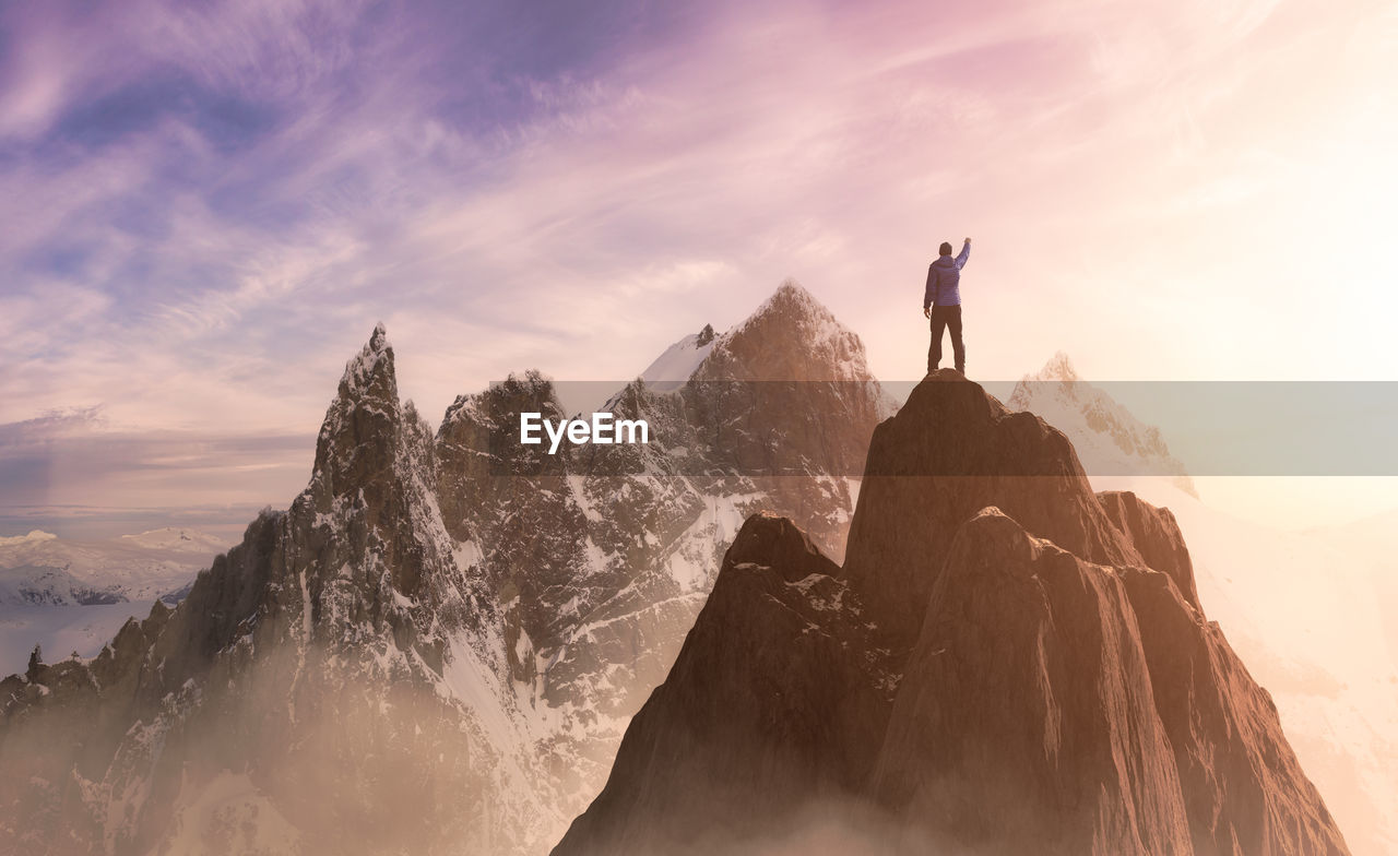 MAN STANDING ON ROCKS AGAINST MOUNTAIN RANGE