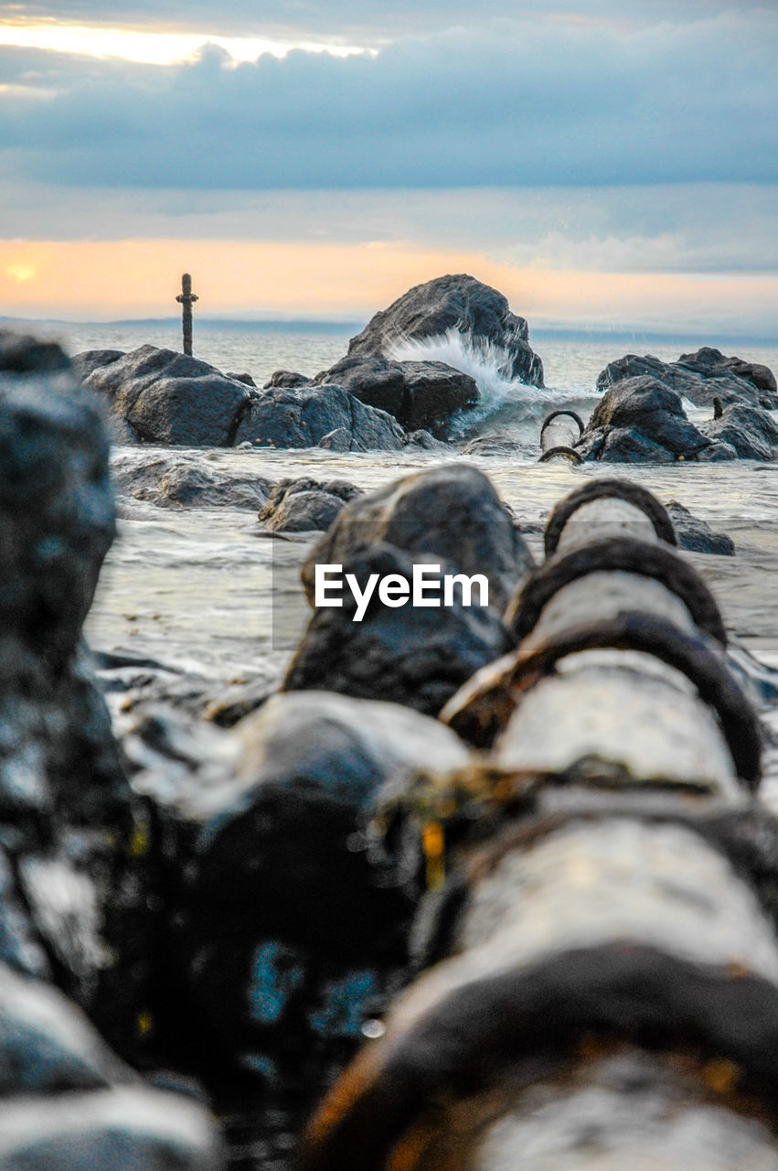 Close-up of pipe running into sea against sky at sunset