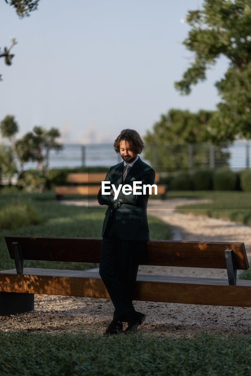 side view of young man sitting on bench against trees