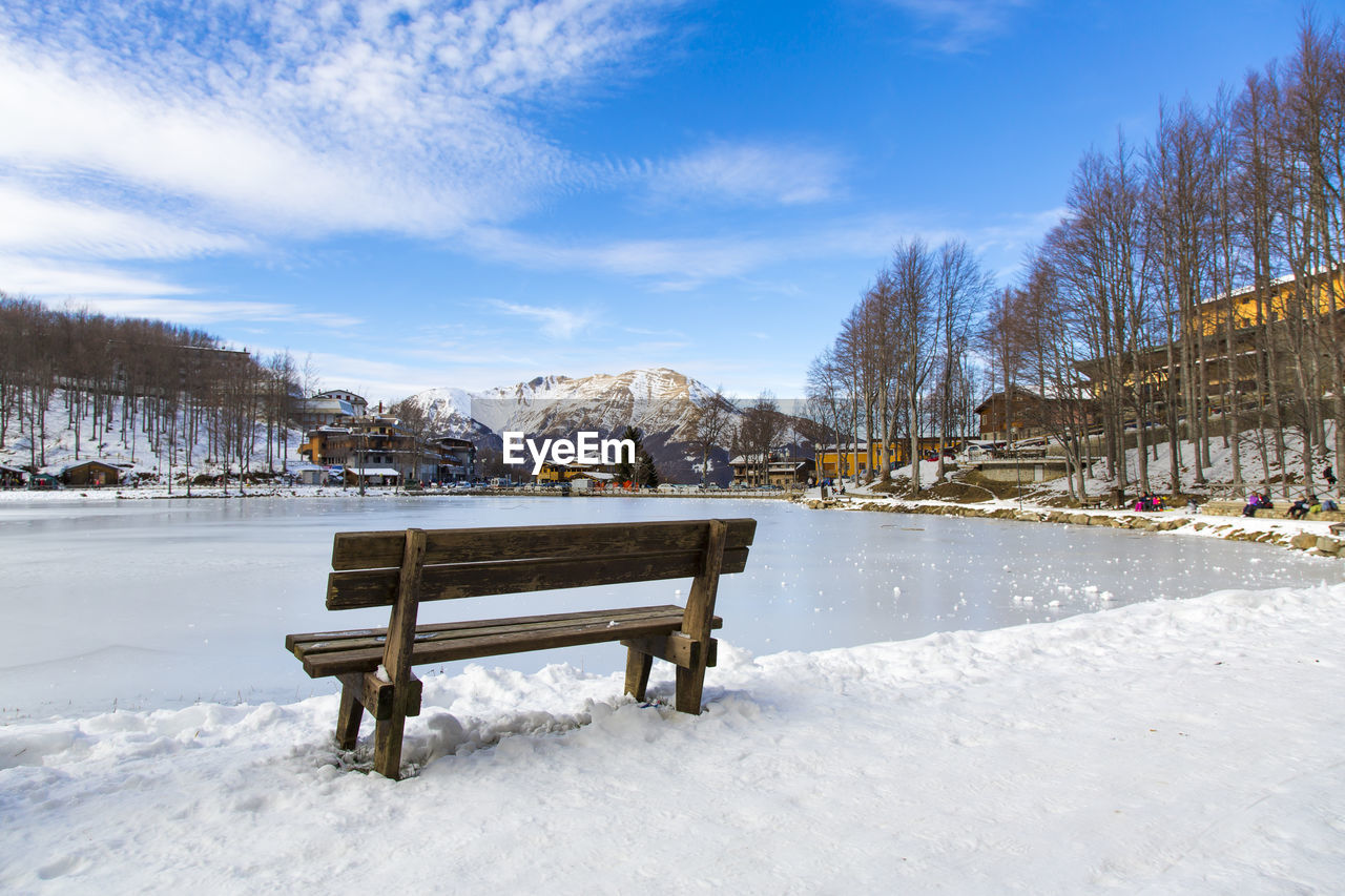 Benche on snow covered bench against sky