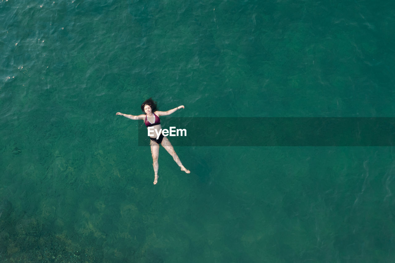 Woman with swimsuit floating and swimming in blue sea. overhead shot. aerial drone photograph