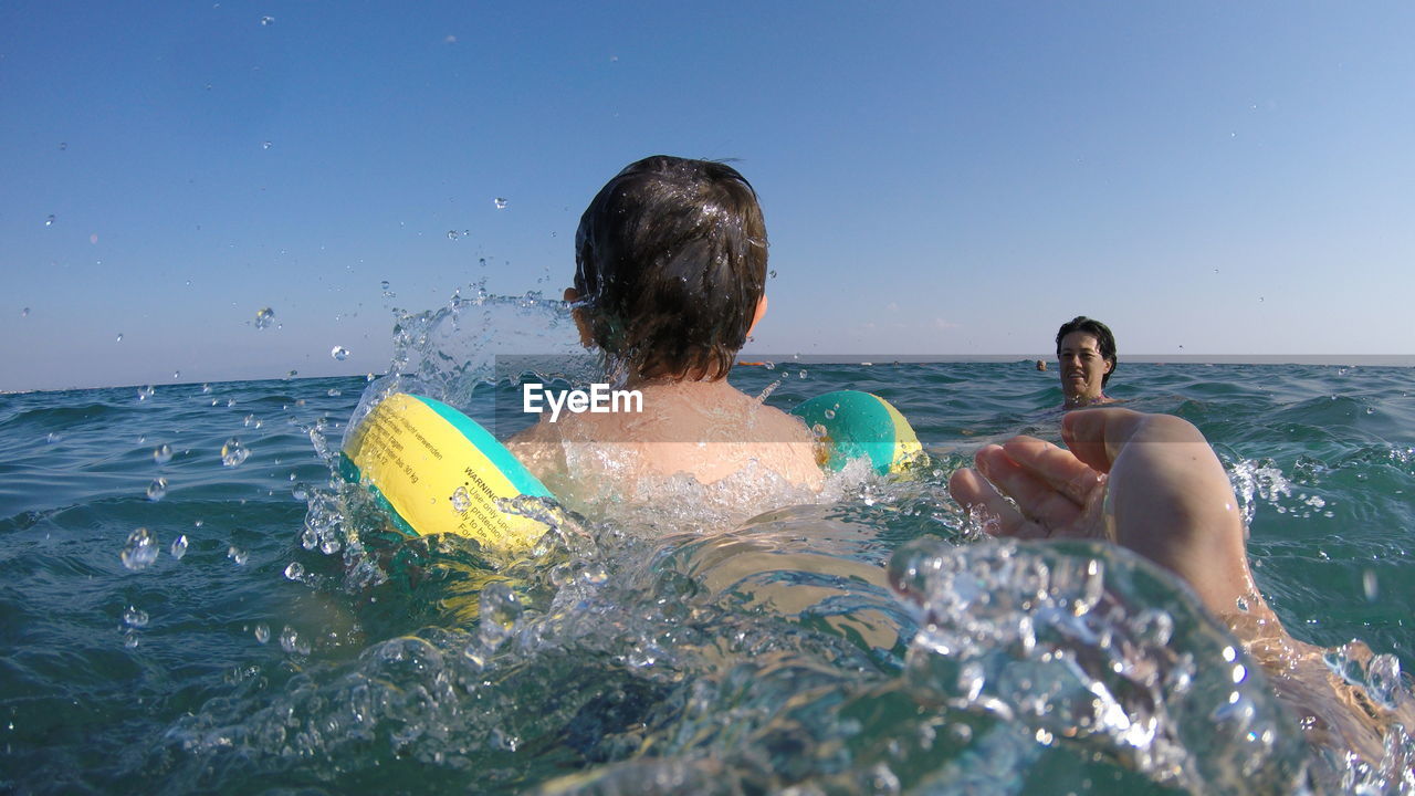 Father and son swimming in sea against clear sky