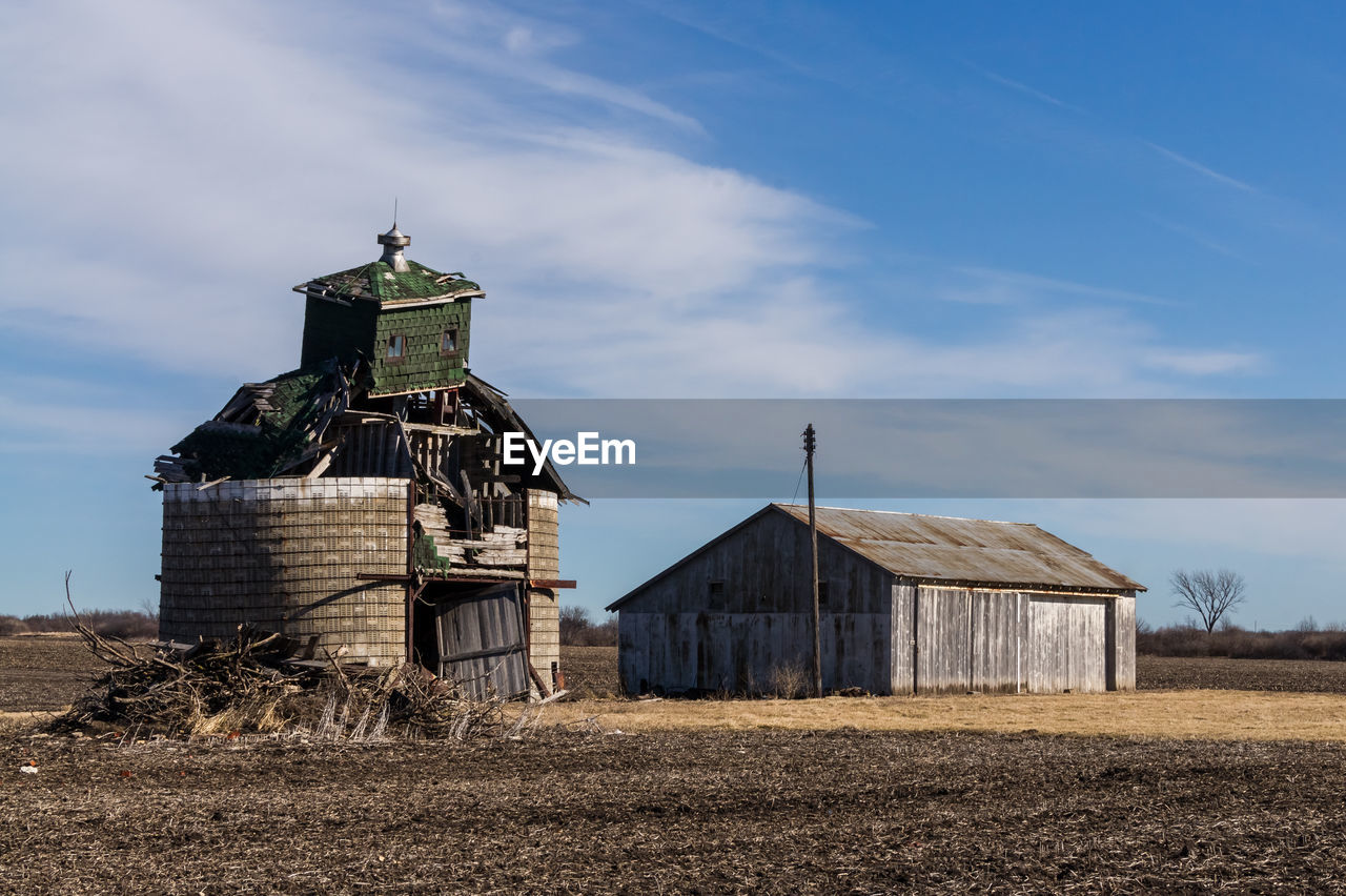 Barn by abandoned built structure on field against sky