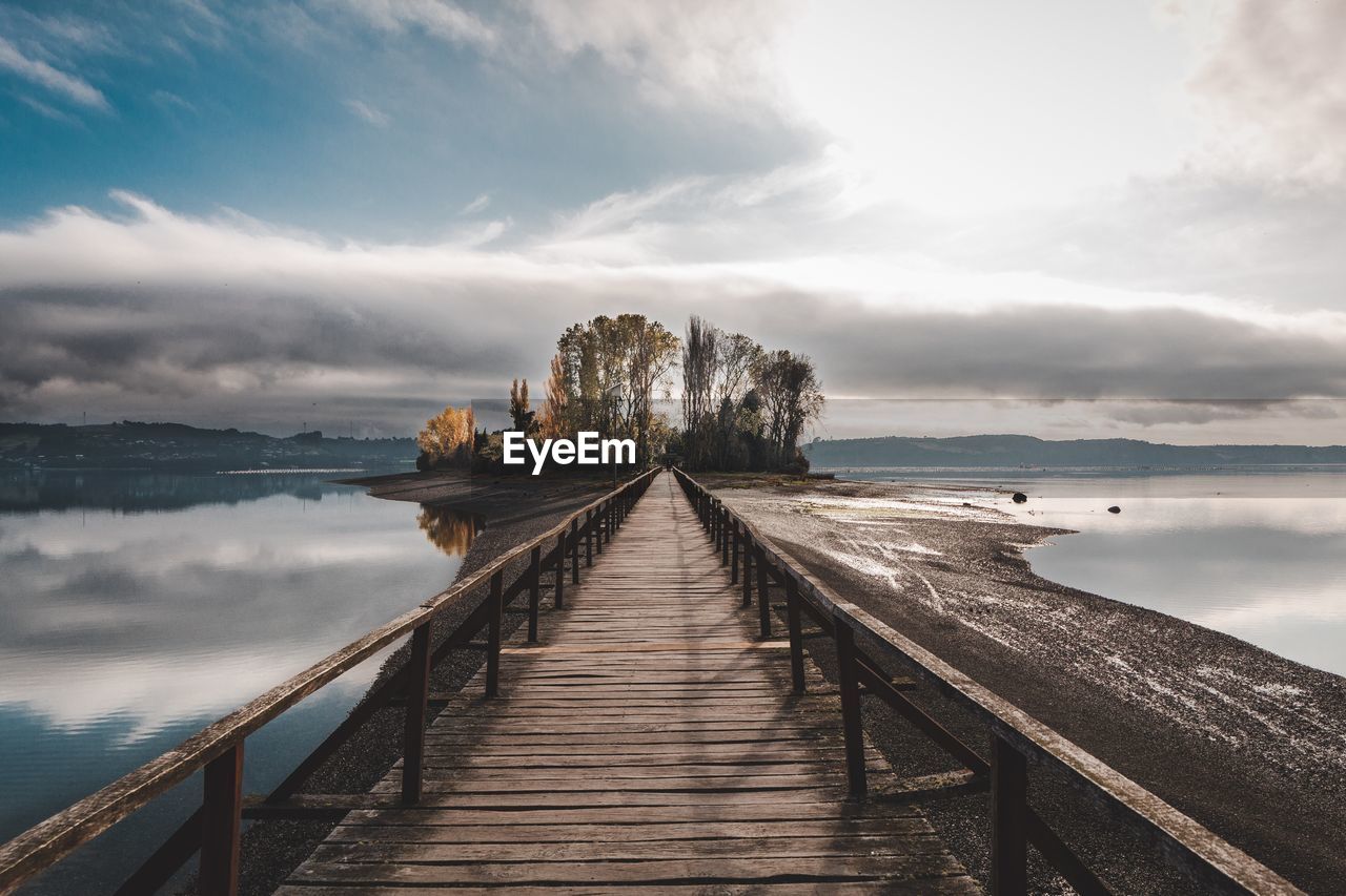 Footbridge by lake against sky