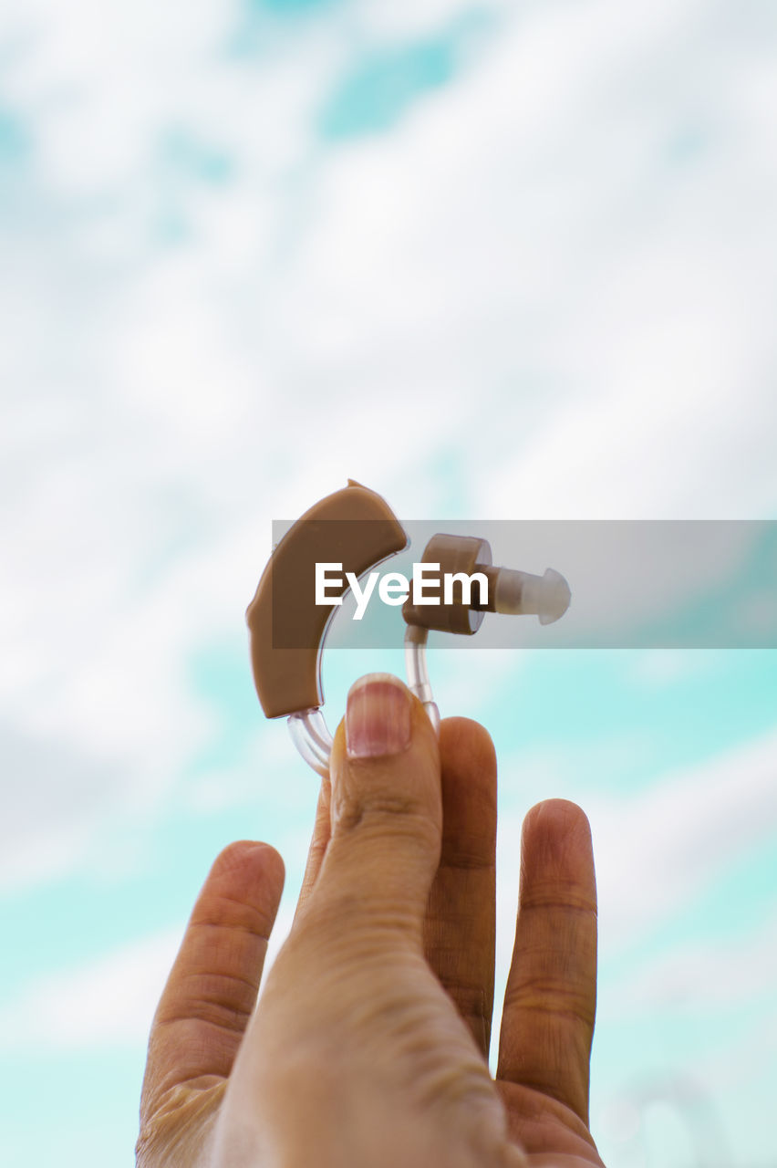 Cropped hands of person holding hearing aid against sky