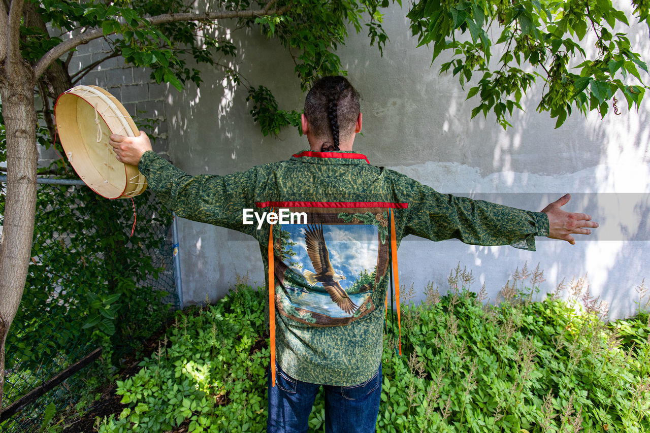 REAR VIEW OF MAN STANDING BY TREE