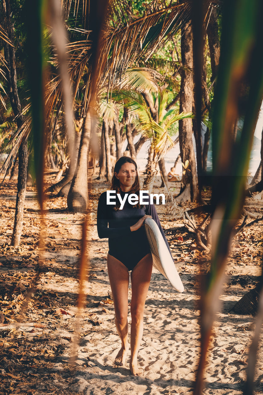 Full length of mature woman with surfboard walking at beach