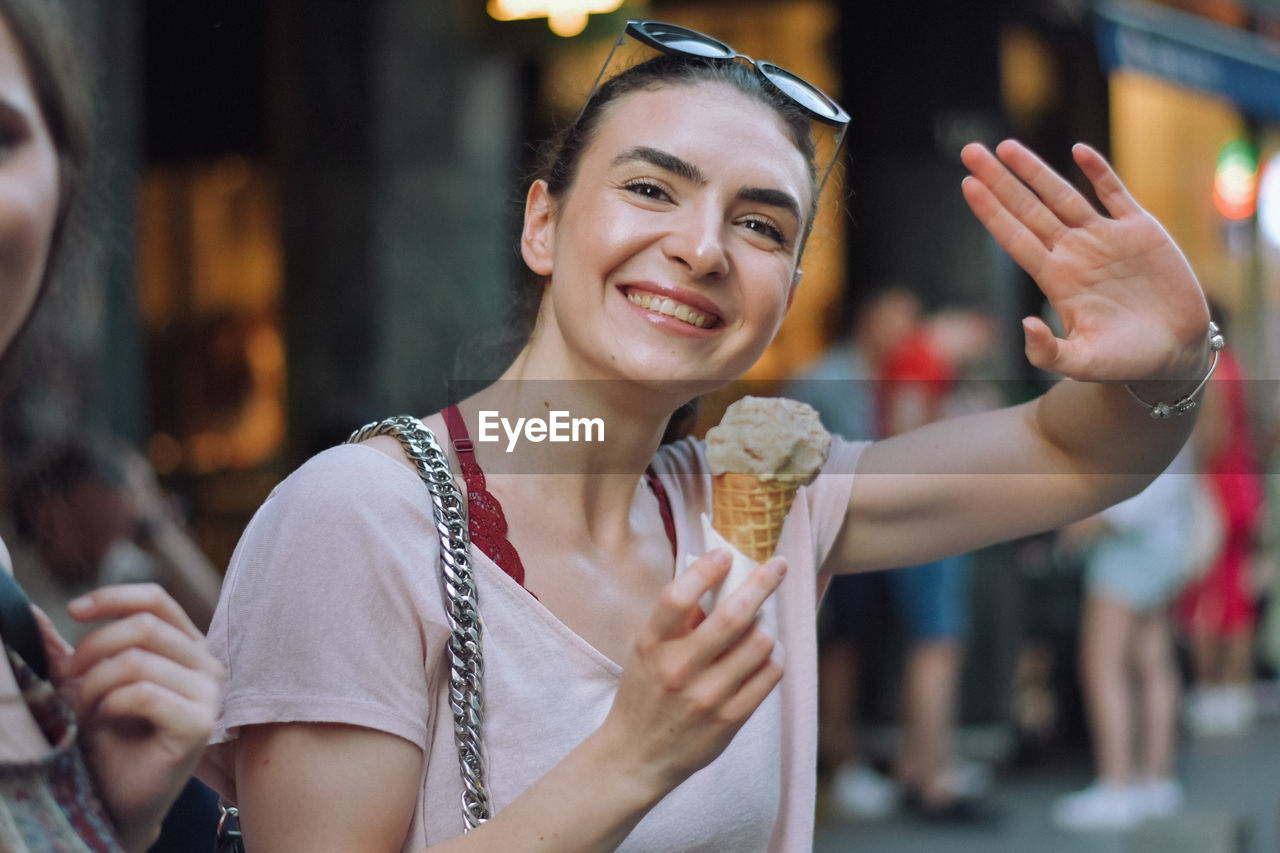 smiling, happiness, women, adult, city, portrait, emotion, cheerful, young adult, city life, enjoyment, street, lifestyles, food and drink, person, architecture, holding, leisure activity, female, fast food, communication, store, fun, food, sweet food, one person, sweet, retail, front view, outdoors, arts culture and entertainment, waist up, looking at camera, focus on foreground, positive emotion, tourist, casual clothing, celebration, business, tourism, friendship, city street, headshot, wireless technology, smile, ice cream