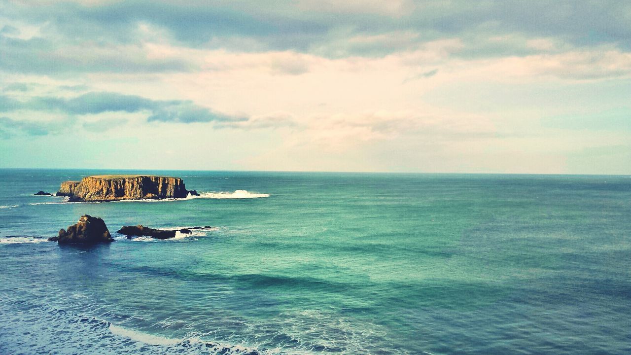 Cliff in sea against cloudy sky