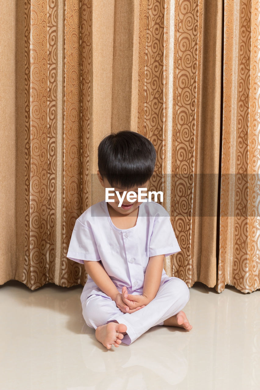 Boy sitting against curtain at home