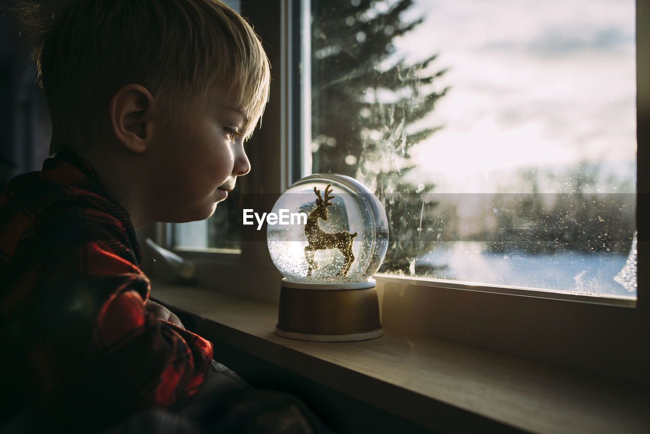 Side view of boy looking at decor on window sill at home