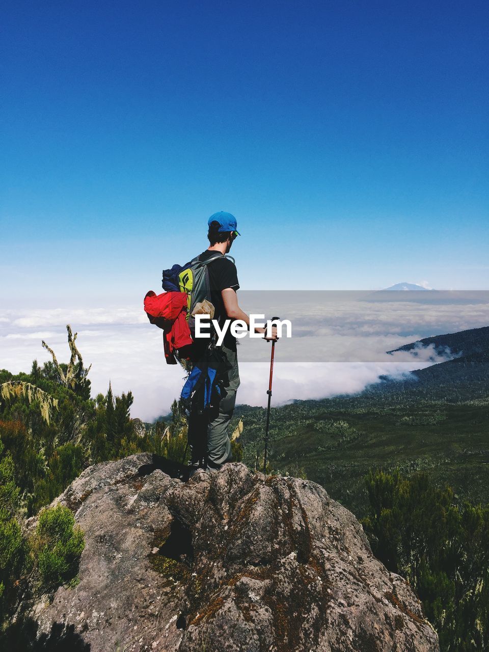 Rear view of hiker on rock looking at clouds covered landscape against sky