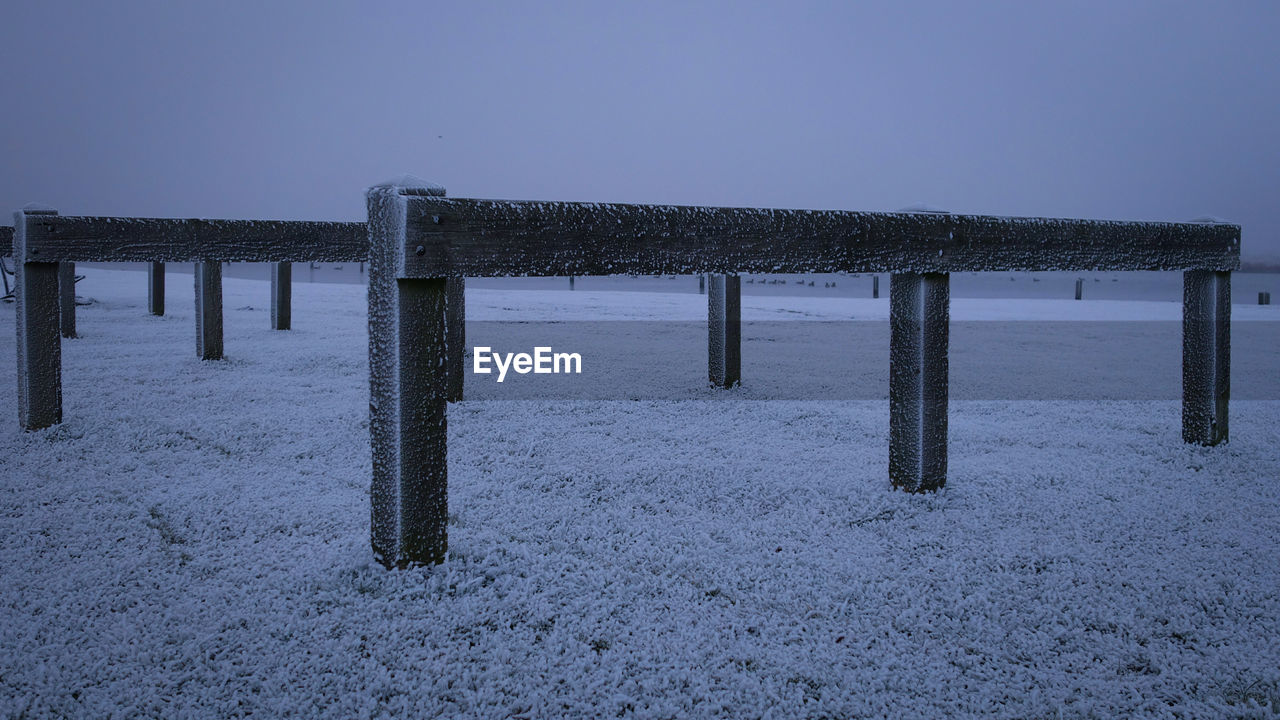 Wooden posts in sea against clear sky during winter
