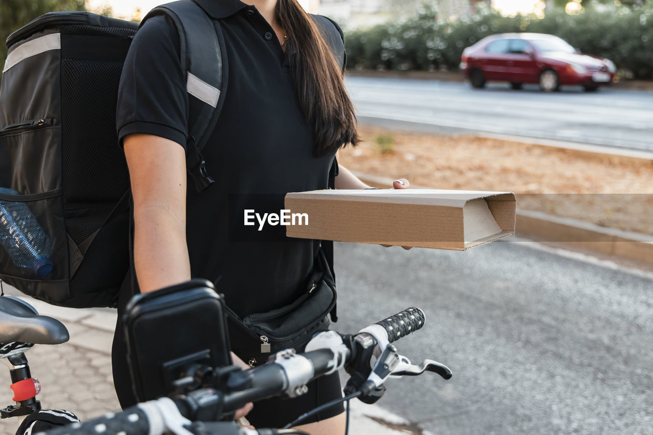 Female essential worker holding courier package while wheeling cycle