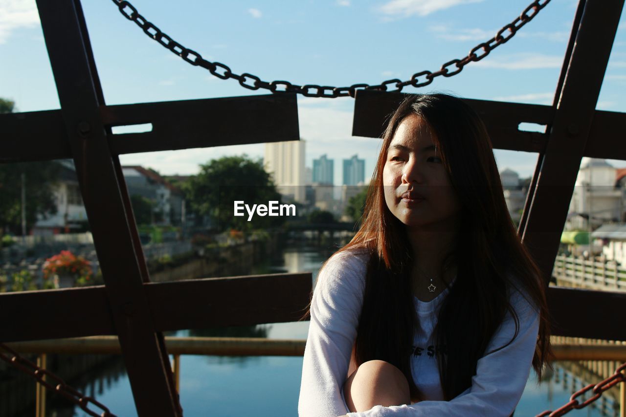 Thoughtful young woman sitting on bridge in city