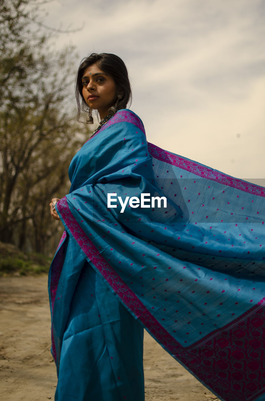 Portrait of beautiful woman wearing sari while standing against trees and sky