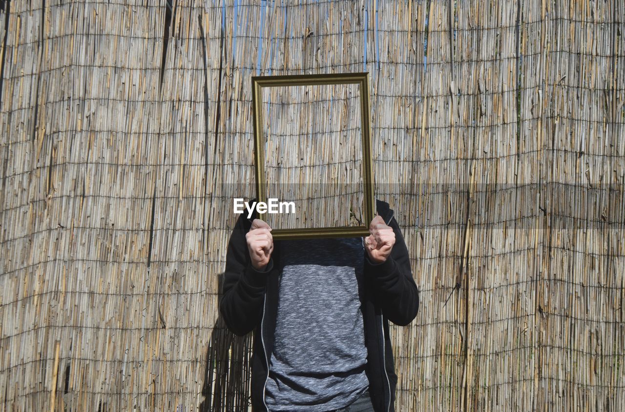 Close-up of man holding frame and standing against wall