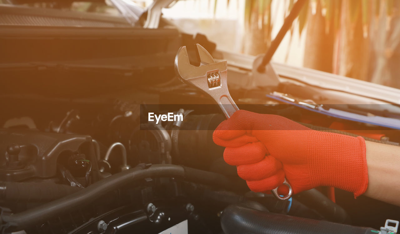 Cropped hand of mechanic holding wrench against car engine