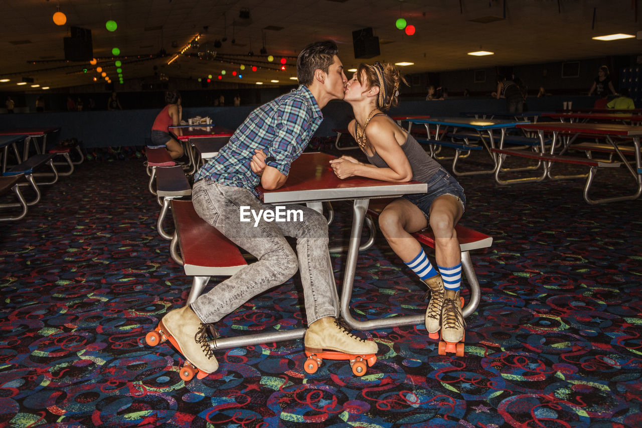 Couple wearing roller skates kissing while sitting at table in club