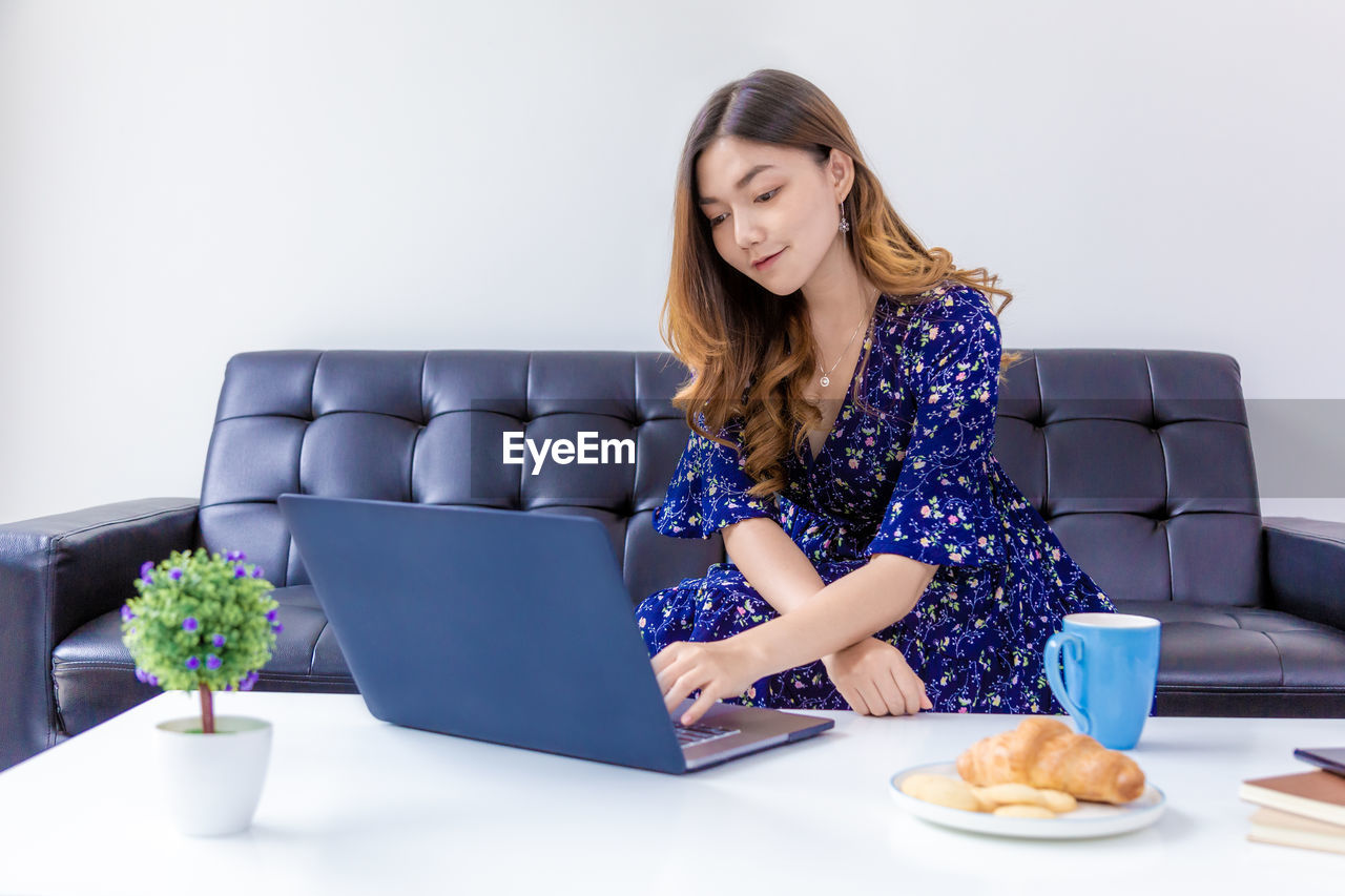 YOUNG WOMAN USING SMART PHONE WHILE SITTING IN LAPTOP