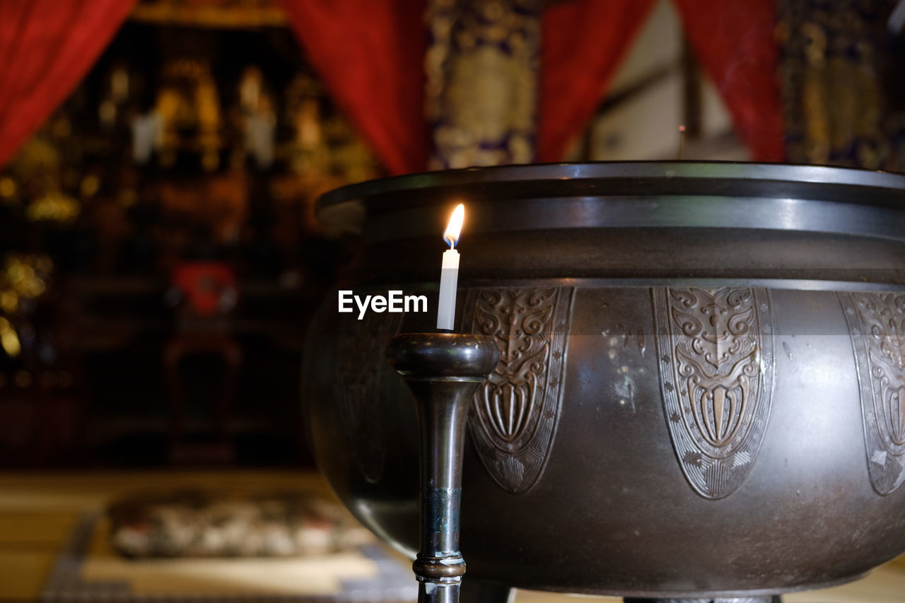 Close-up of lit candle and container in church