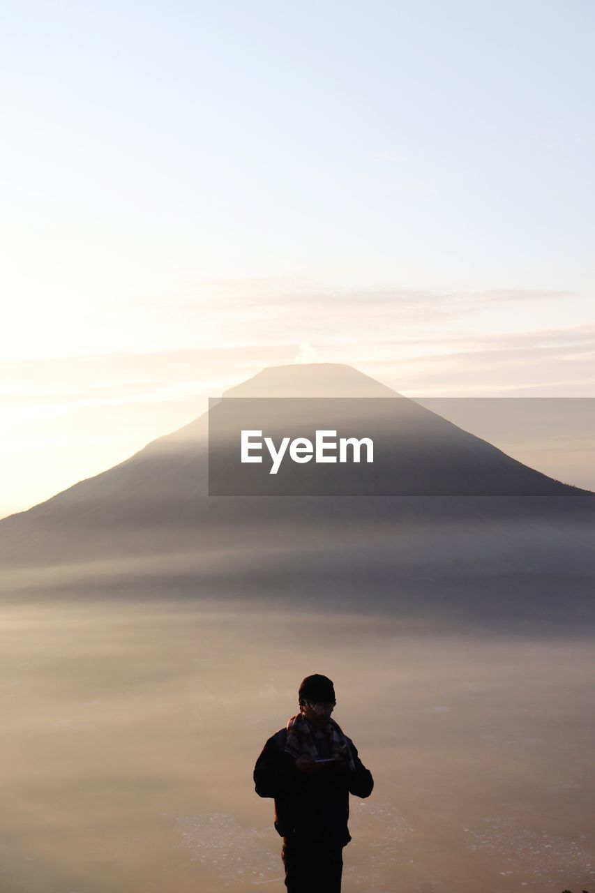 Rear view of man standing on mountain against sky