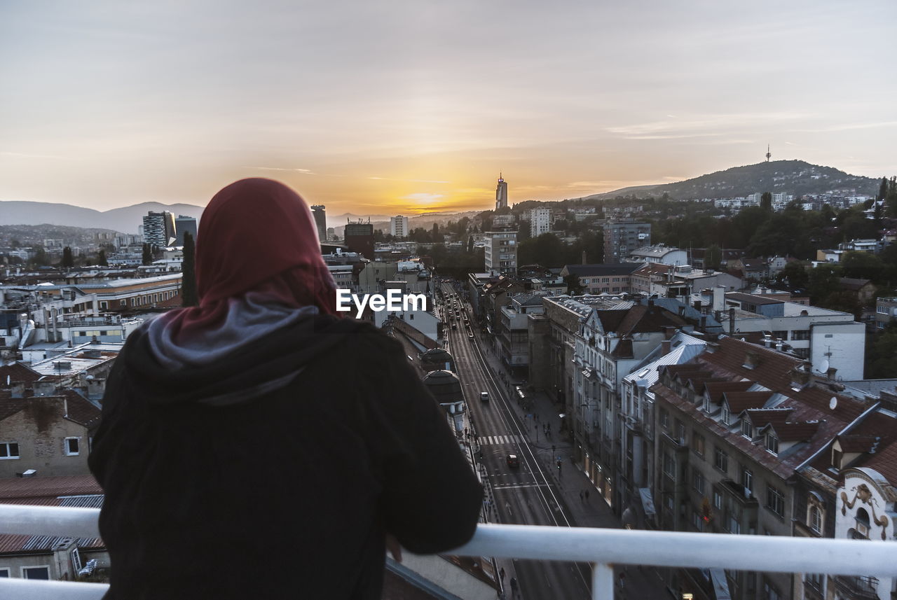 REAR VIEW OF MAN LOOKING AT CITY AGAINST SKY