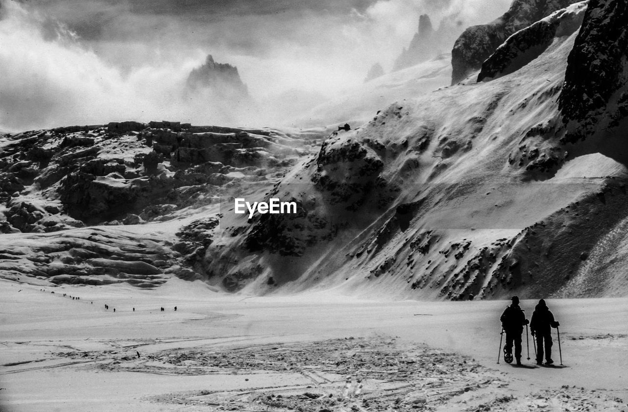 Hikers on snow covered mountain against sky